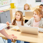 Schüler mit Laptop und Tablet im Klassenzimmer hören Lehrer zu