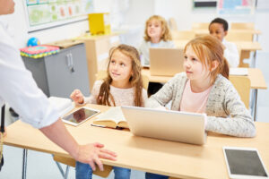 Schüler mit Laptop und Tablet im Klassenzimmer hören Lehrer zu