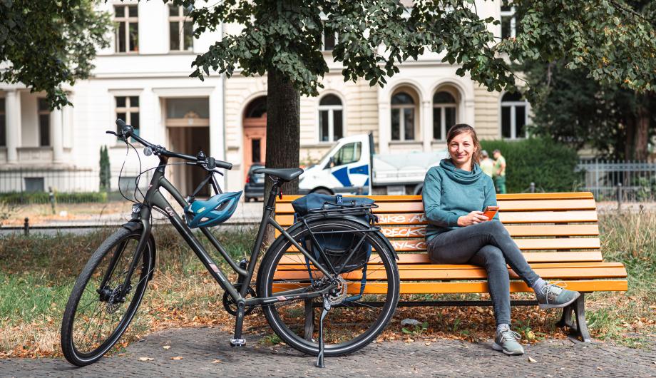 Frau mit Fahrrad sitzt auf einer Bank