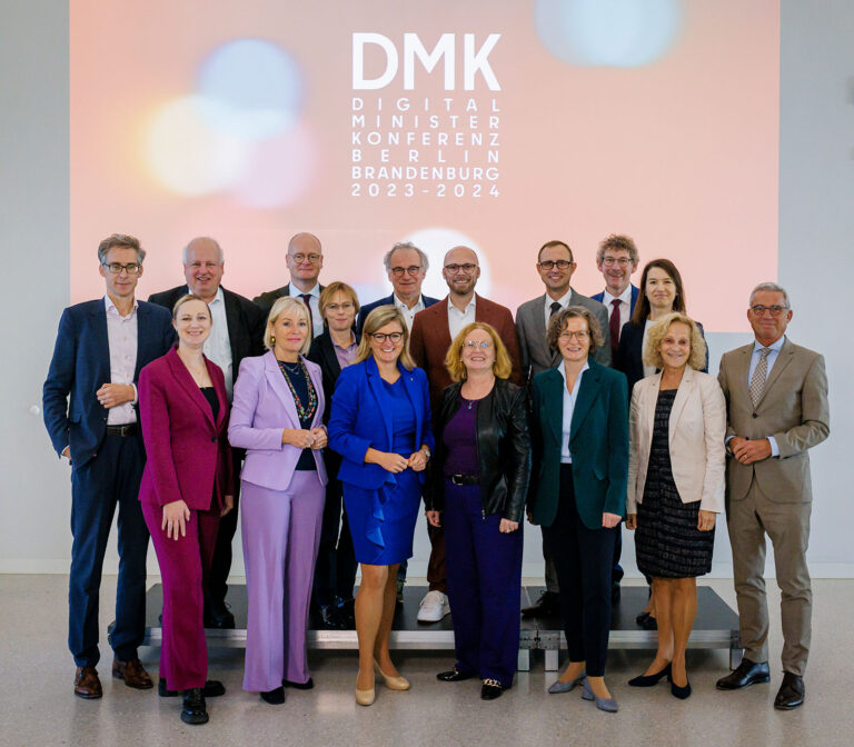 Gruppenfoto der Digitalverantwortlichen der Länder vor einer Projektion mit DMK-Logo.