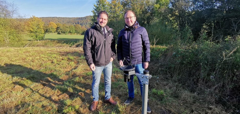 Lauritz Drechsler vom Smart City Team des Landkreises Hameln-Pyrmont und Thomas Rahne, Klimafolgenanpassungs-Manager der Stadt Bad Pyrmont bei der Installation eines digitalen Regensensors im Grünen. 