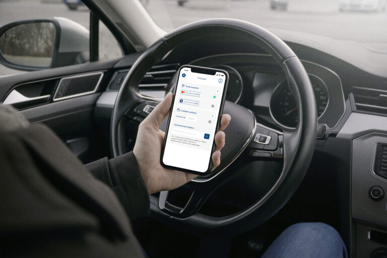 Mann sitzt am Steuer seines Fahrzeugs und hält ein Mobiltelefon mit der Handypark-App mobilet in der Hand