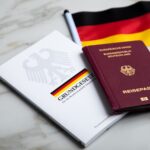 Ein deutscher Reisepass, das deutsche Grundgesetzbuch und eine Deutschlandflagge liegen auf einer marmorierten Unterlage.