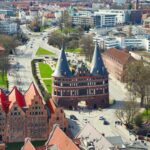 Blick von schräg oben auf den Lübecker Holstentorplatz und Umgebung, im Zentrum das backsteinerne Holstentor mit Kupferdach.