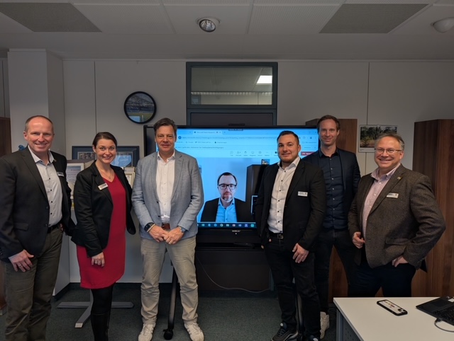 Gruppenfoto das (v.l.) Bürgermeister Tobias Handtke, Miriam Rathmann, Tim Beckmann, Stefan Pahmeier (per Videokonferenz auf einem Bildschirm zugeschaltet), Steffen Matthees, Jan Behrenbruch und Partho Banerjea zeigt.