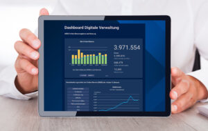 Person mit weißem Hemd hält ein Tablet gegen die Kamera, darauf sind Balkendiagramme zu sehen.