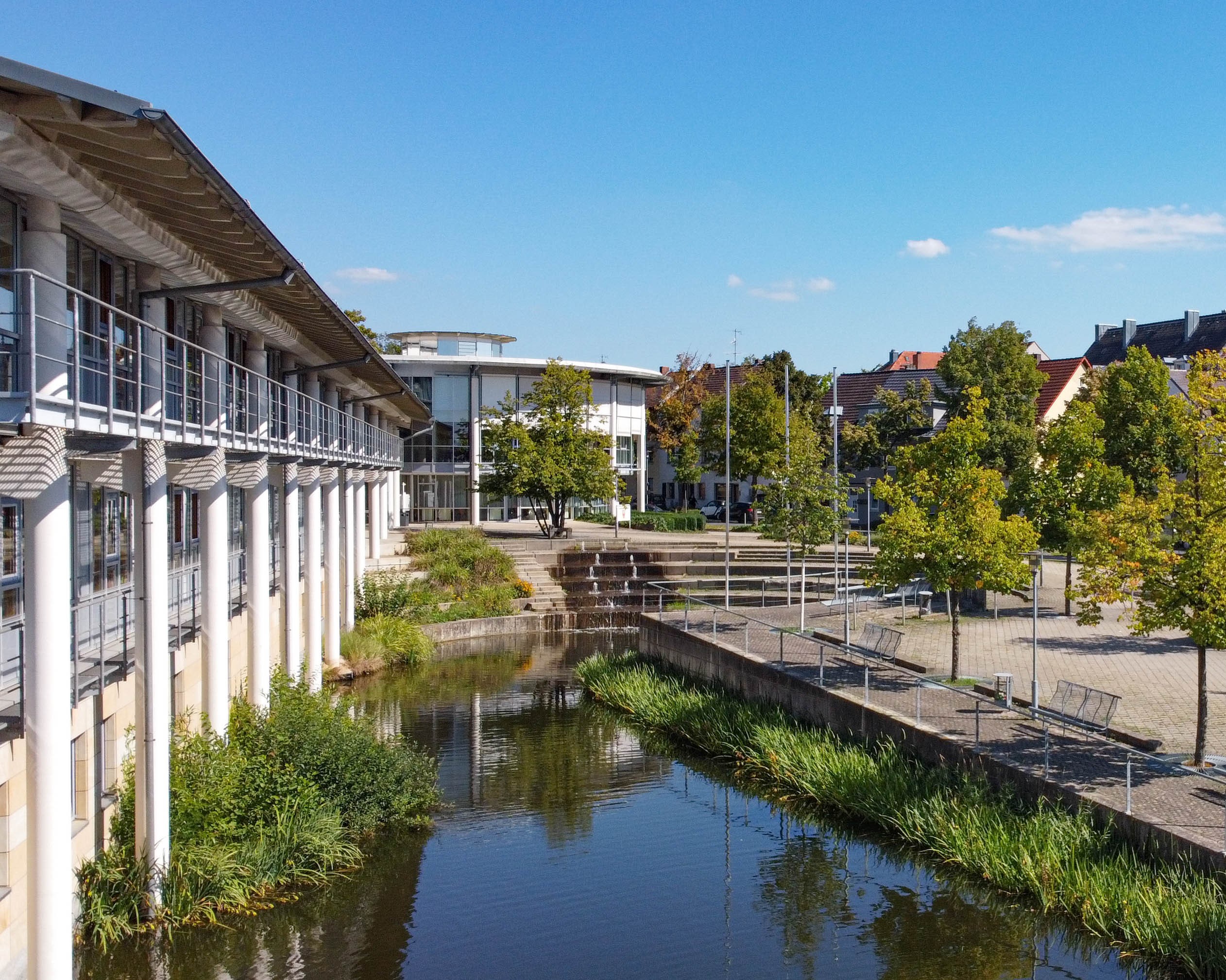 Luftaufnahme des Landratsamts Bayreuth, ein weißes, aus zwei Flügeln bestehendes, circa zweigeschossiges Gebäude an einer Teichanlage.