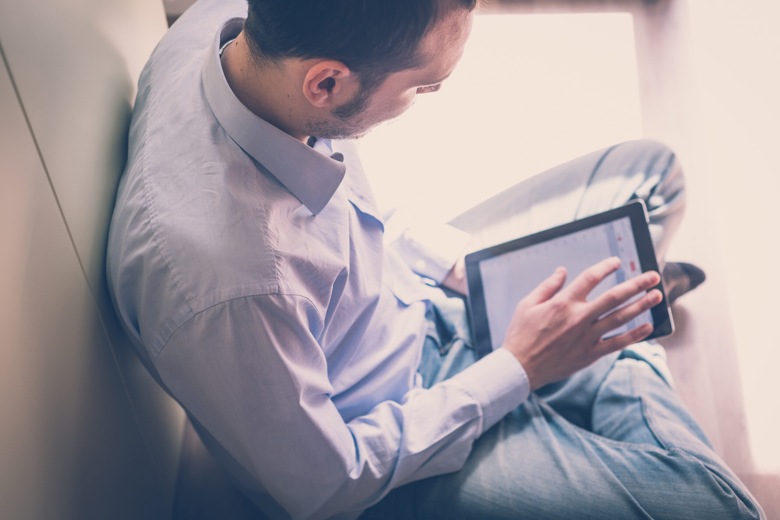 Mann im eleganten Hemd von oben aufgenommen, er hält ein Tablet und tippt darauf..