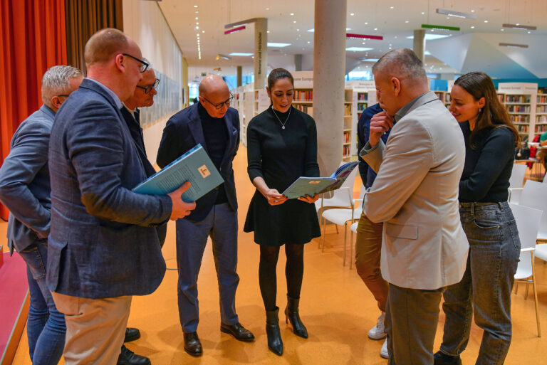 Stadträtin und Digitalisierungsdezernentin Isabelle Hemsley steht mit Mitgliedern des städtischen Lenkungskreises Smart City im Hanauer Kulturforum und blättert in einer Broschüre.