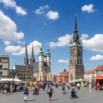 Das Bild zeigt den belebten Markplatz von Halle (Saale), im Hintergrund sind die fünf Türme der Händelstadt zu erkennen.