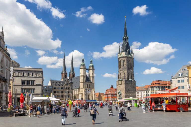 Das Bild zeigt den belebten Markplatz von Halle (Saale), im Hintergrund sind die fünf Türme der Händelstadt zu erkennen.