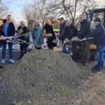 v.l.: Tiemo Papsdorf, Baufirma Kuhlmann; Thomas Barufke und Jessica Rotärmel, Stabsstelle Breitband, Landkreis Osnabrück; Mario Aquino, Netzbetreiber GVG Glasfaser; Dominik Schmidt, Baufirma Kuhlmann; Claudia Pelzl, Netzbetreiber GVG Glasfaser; Landrätin Anna Kebschull; Marco Kreyenhagen, Hof Kreyenhagen; Bürgermeister Erik Ballmeyer, Ostercappeln; Stephan Simon, Stabsstelle Breitband, Landkreis Osnabrück. Sie halten Schaufeln in der Hand und werfen damit Aushubmaterial, das zu einem Berg aufgehäuft zwischen ihnen liegt, in die Luft. Im Hintergrund ist ein kleiner Bagger zu sehen.