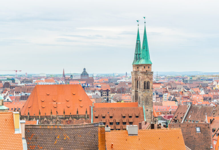 Luftbild der Nürnberger Altstadt: viele rote Ziegeldächer, im Bildzentrum der grüne Doppelturm von St. Sebaldus.