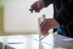 Hand steckt Wahlzettel in eine Wahlurne.