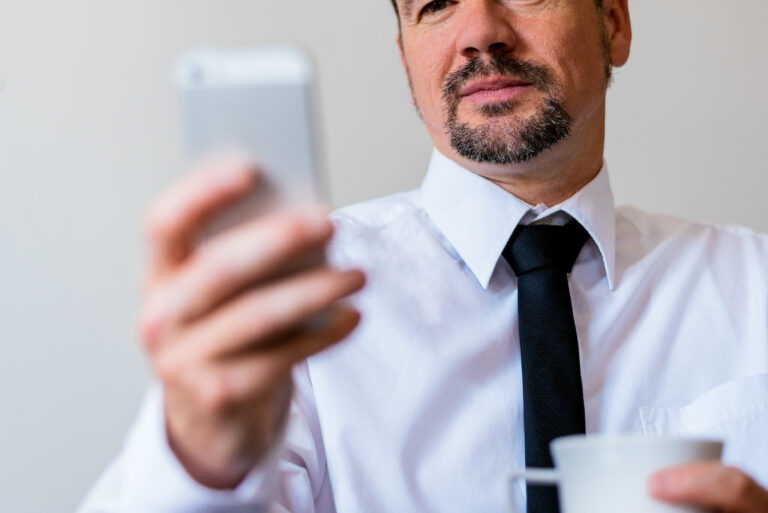 Mann mit Hemd und Schlips schaut auf sein Smartphone.