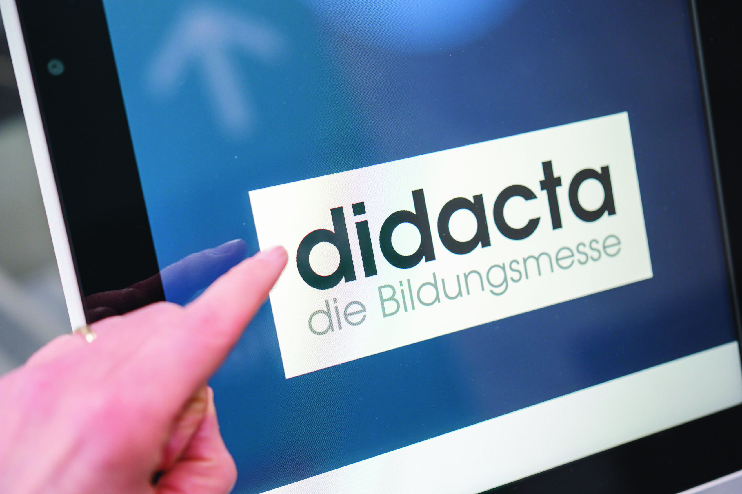 Ein Finger zeigt auf einen Schriftzug der Bildungsmesse didacta auf einem Touchscreen.