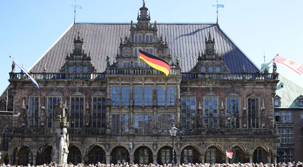 Rathaus der Freien und Hansestadt Bremen, mit Arkaden und drei markanten Stufengiebeln, Deutschlandflagge wehtt, blauer Himmel.