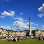 Stuttgarter Schlossplatz mit Jubiläumssäule bei gutem Wetter, Menschen sitzen auf der Wiese.