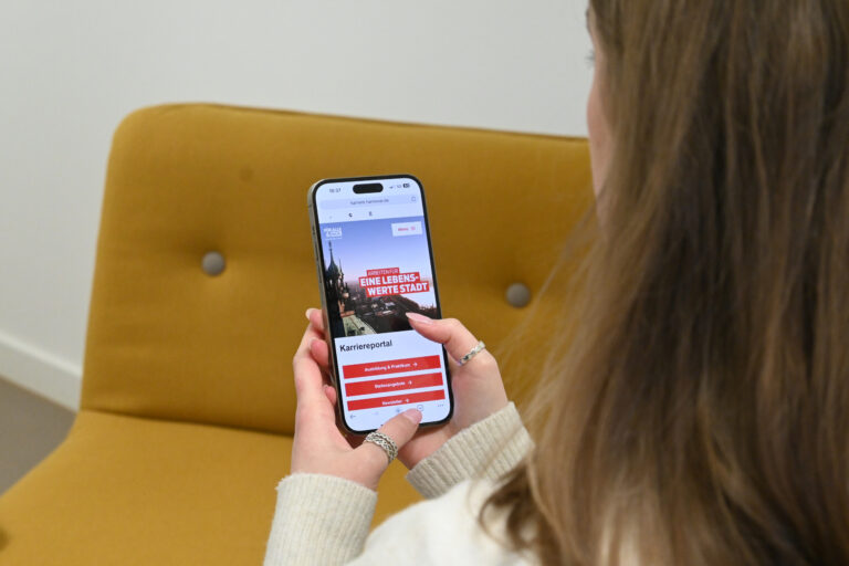 Eine Frau hält ein Smartphone in der Hand, das das Karriereportal der Stadt Hannover anzeigt.