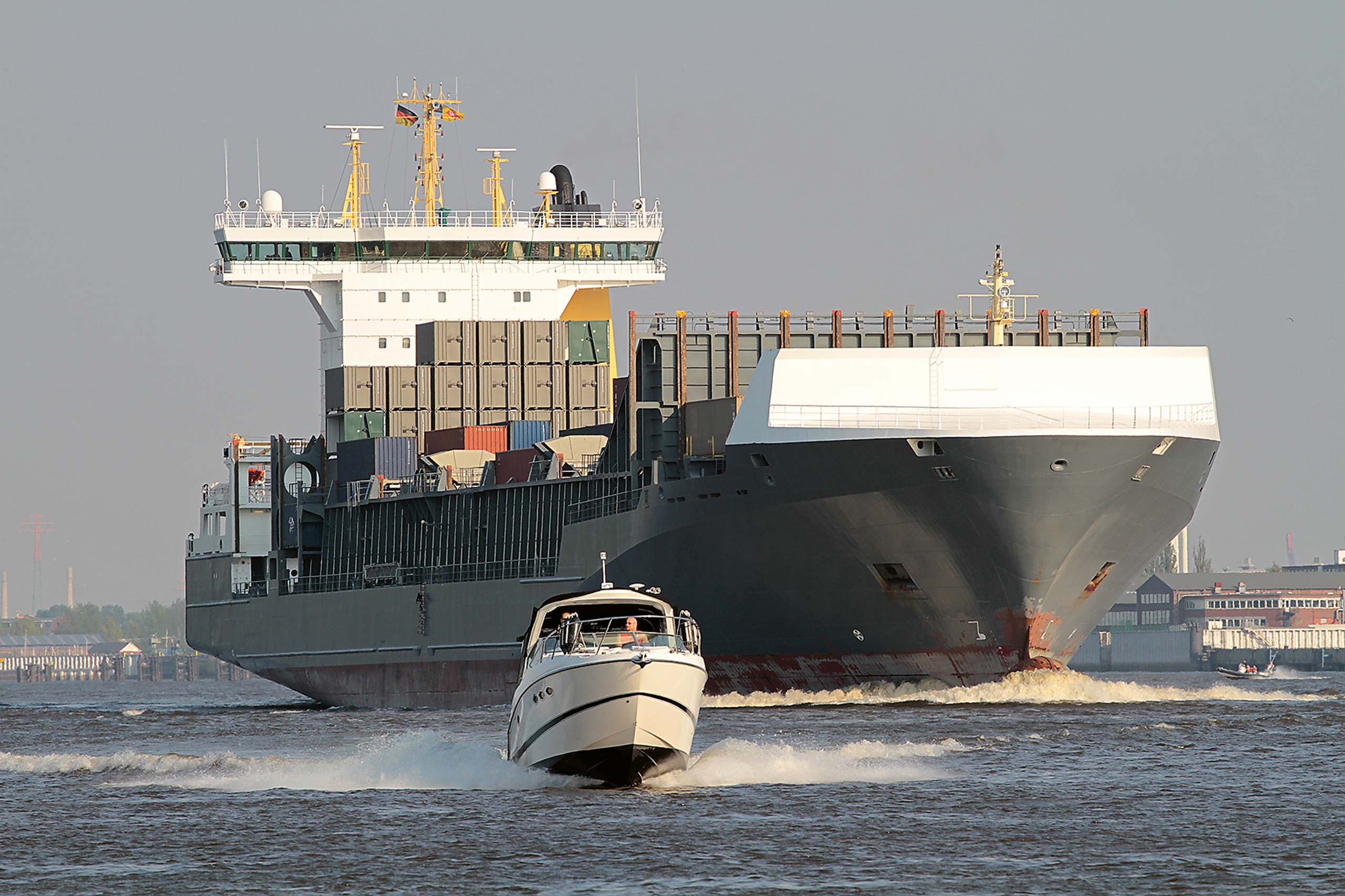 Großes Frachtschiff, davor fährt ein kleines Motorboot.