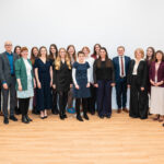 Gruppenfoto von Männern und Frauen in Businesskleidung in einem weißen Innenraum mit Holzboden.