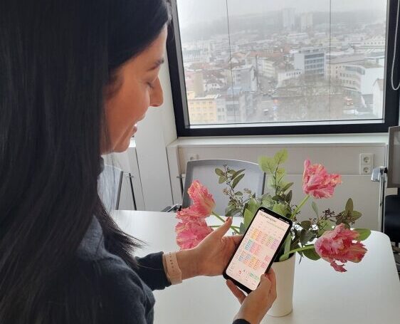 Person mit langen dunklen Haaren in einem Zimmer sieht auf ihr Smartphone.