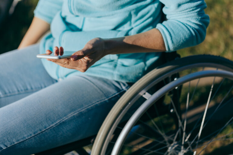 Eine Frau im Rollstuhl hält ein Smartphone in der Hand.