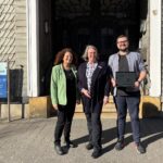 Manuela Marxen, Claudia Wiegelmann und Pascal Stewin stehen nebeneinander vor einem Gebäude, Stewin hält einen aufgeklappten Laptop in der Hand.